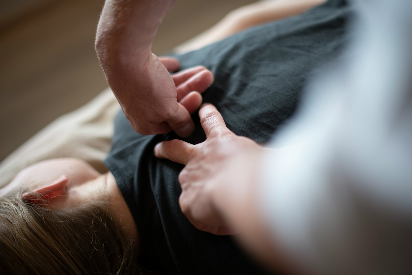 Hände führen eine therapeutische Justierung am oberen Rücken einer Person durch.